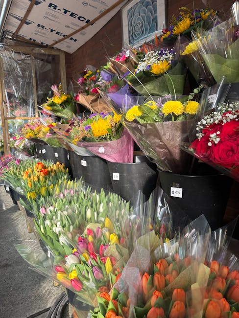 An array of fresh floral bouquets arranged in black buckets inside a florist shop, featuring a variety of colorful flowers including yellow chrysanthemums, pink and purple tulips, red roses, white bab
