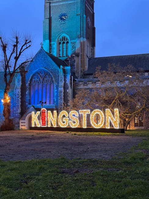A nighttime scene featuring a church with gothic architecture illuminated by blue lighting, with bare trees in the foreground. Below the church, a large, colorful sign spelling 'KINGSTON' in illuminat